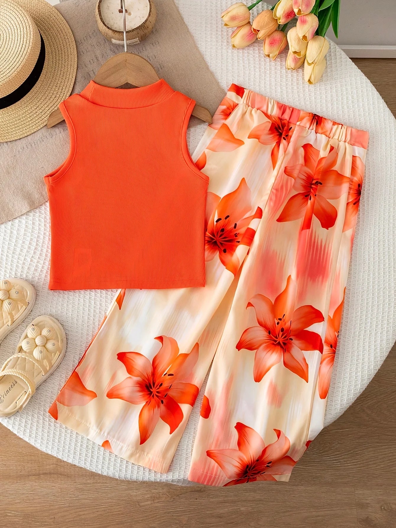 Girls' orange vacation-style two-piece set: a solid-color, ribbed, sleeveless mock-neck crop top paired with lily-print, flowy w