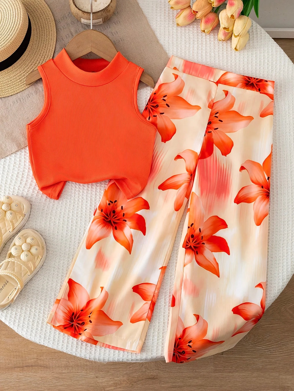 Girls' orange vacation-style two-piece set: a solid-color, ribbed, sleeveless mock-neck crop top paired with lily-print, flowy w