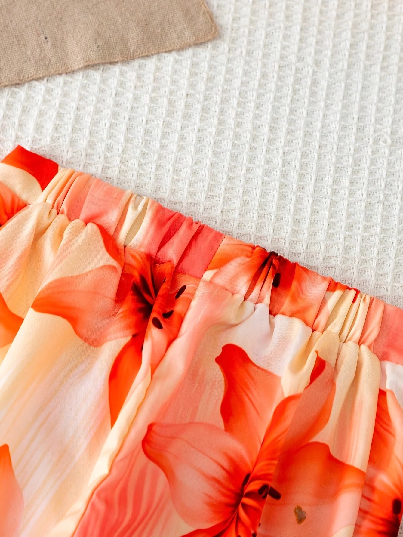 Girls' orange vacation-style two-piece set: a solid-color, ribbed, sleeveless mock-neck crop top paired with lily-print, flowy w